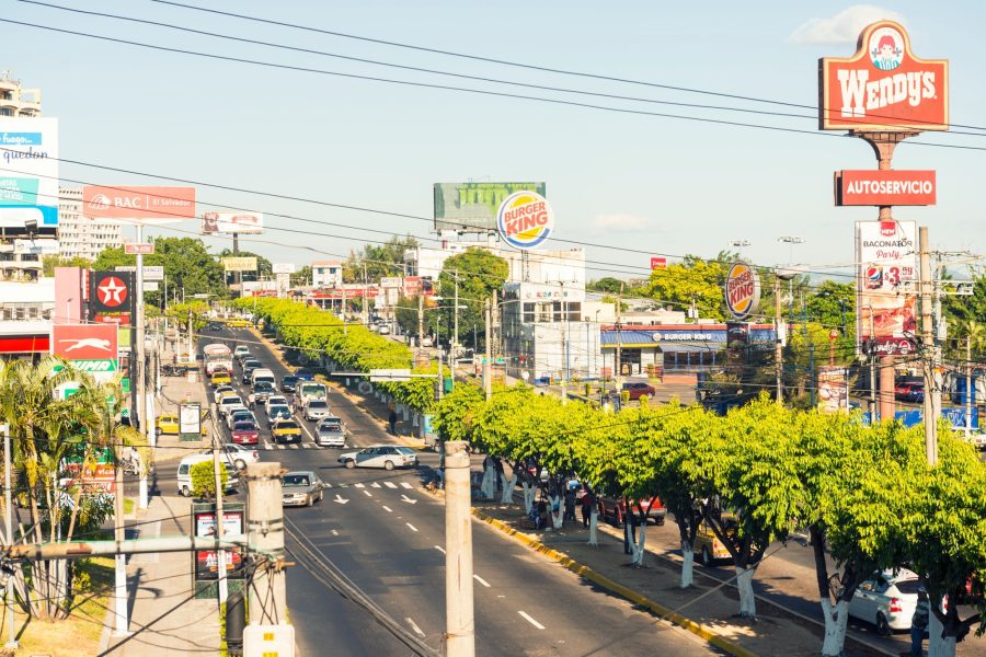 San Salvador in capital city of El Salvador. It is located in highlands  surrounded by volcanoes. View on the main street with car traffic, line of trees and large billboards.